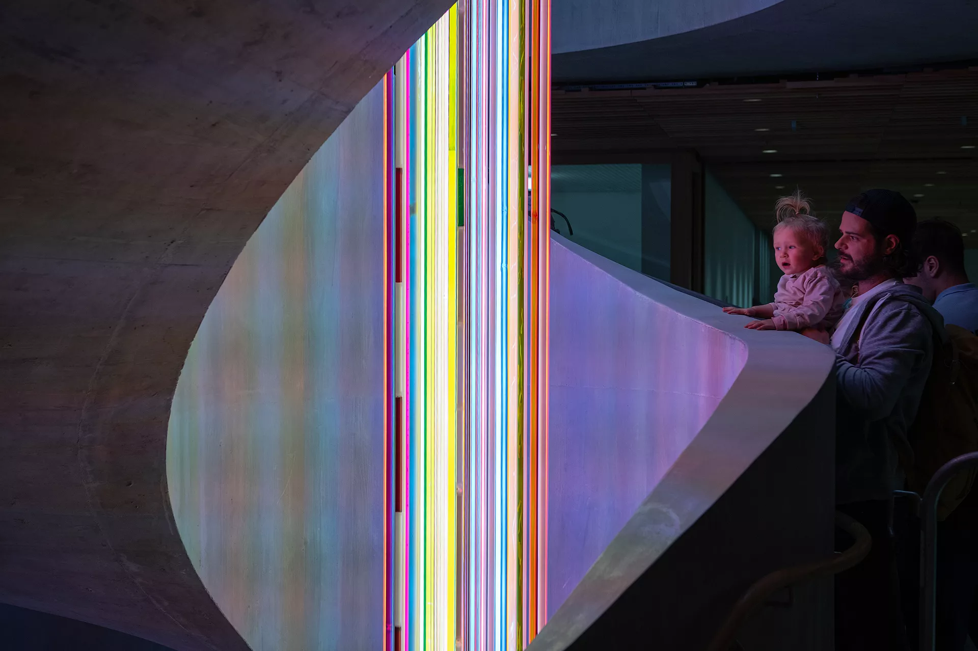 Ein Mann und ein Kind schauen auf farbige Lichtröhren in einem Treppenhaus im Akutspital des Kinderspitals Zürich