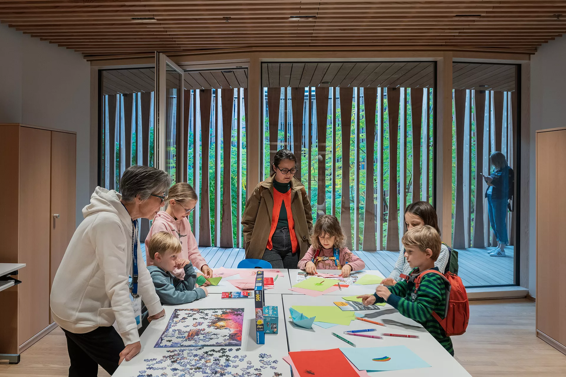 Erwachsene und Kinder stehen an einem Tisch mit Puzzlen, Papier und Stiften