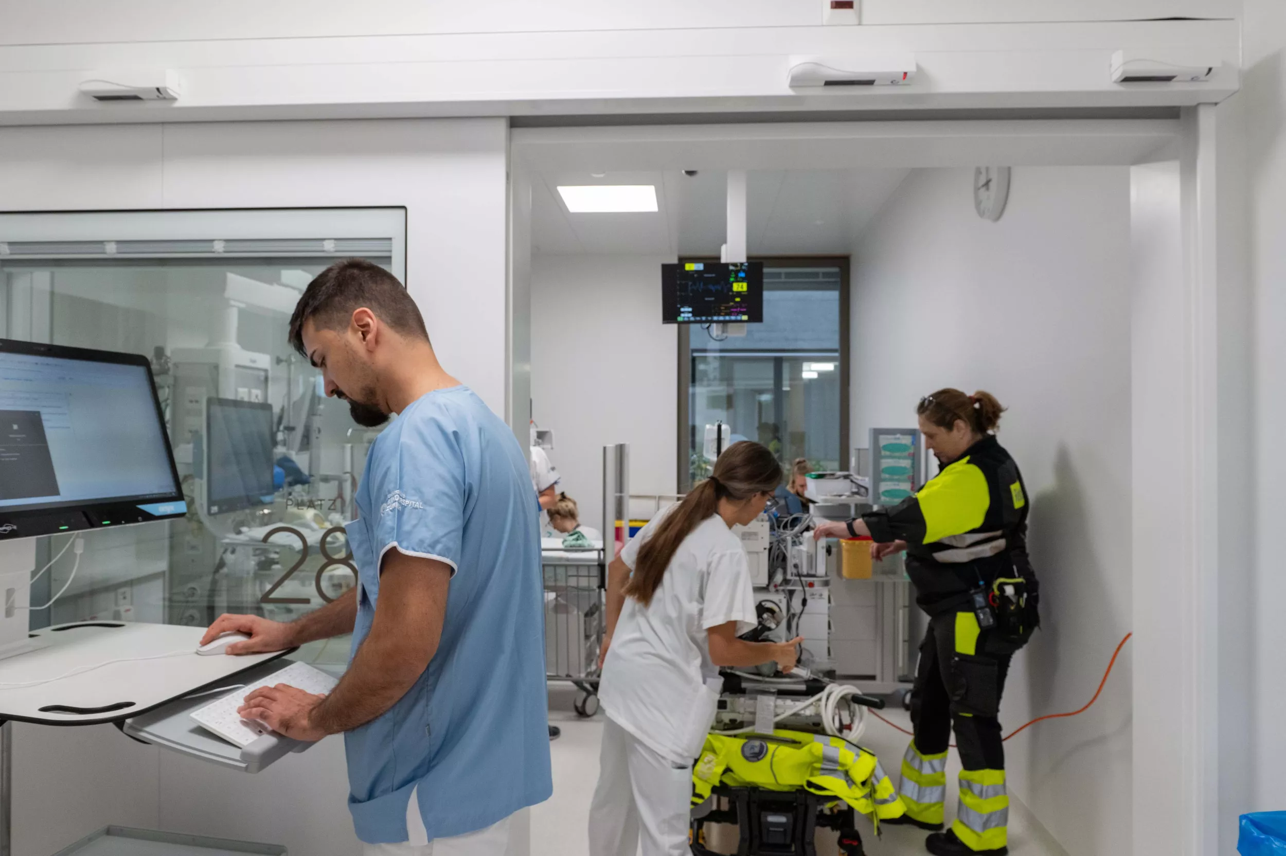 Medizinisches Personal und eine Rettungssanitäterin stehen in einem Behandlungszimmer