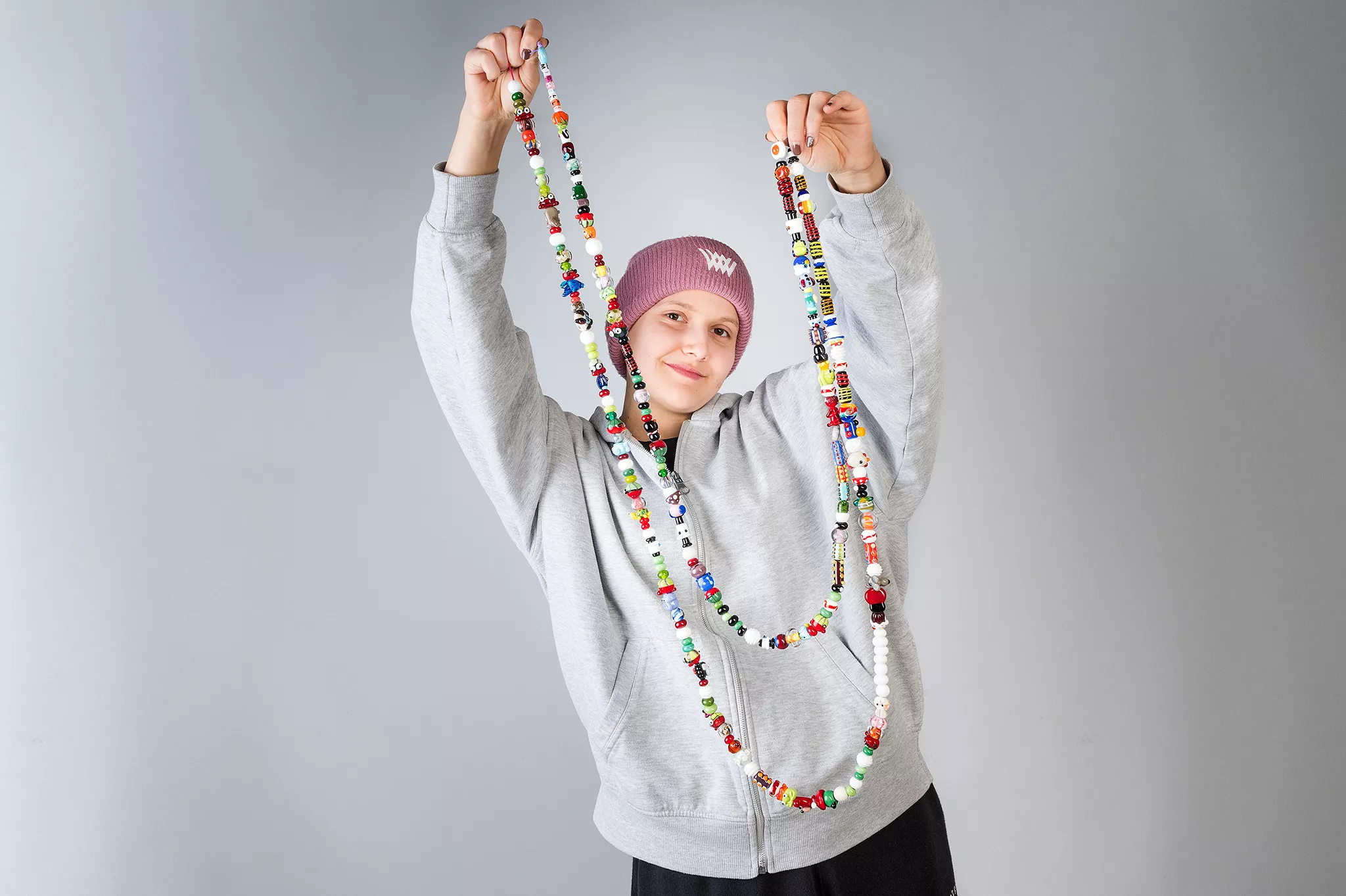 Eine Onkologiepatientin trägt eine Mütze und einen Pullover. Sie steht und hält eine Perlenkette mit sogenannten "Mutperlen" in die Luft.