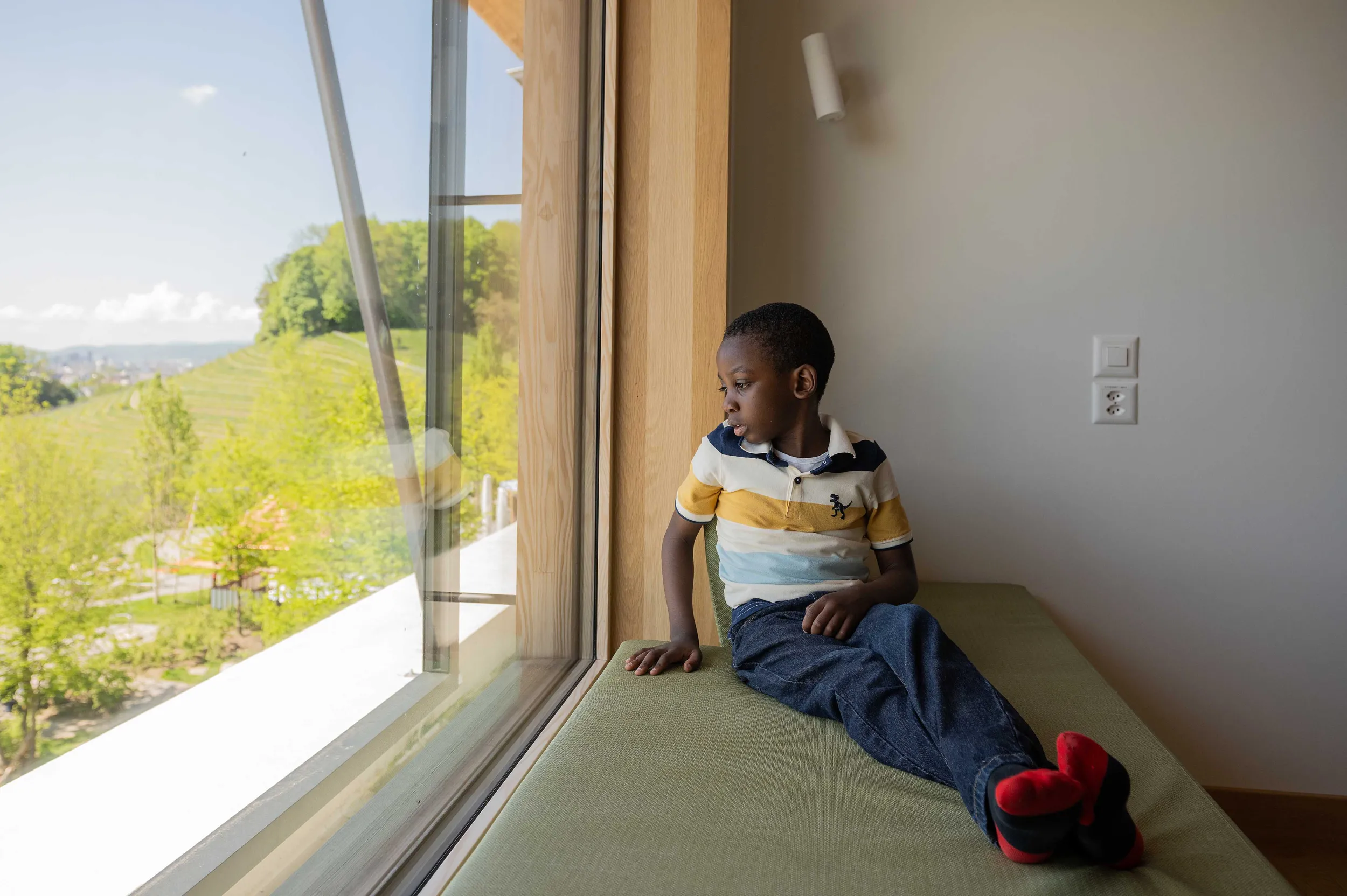 Patient David sitzt auf einem Elternbett und blickt aus dem Fenster im Kinderspital Zürich