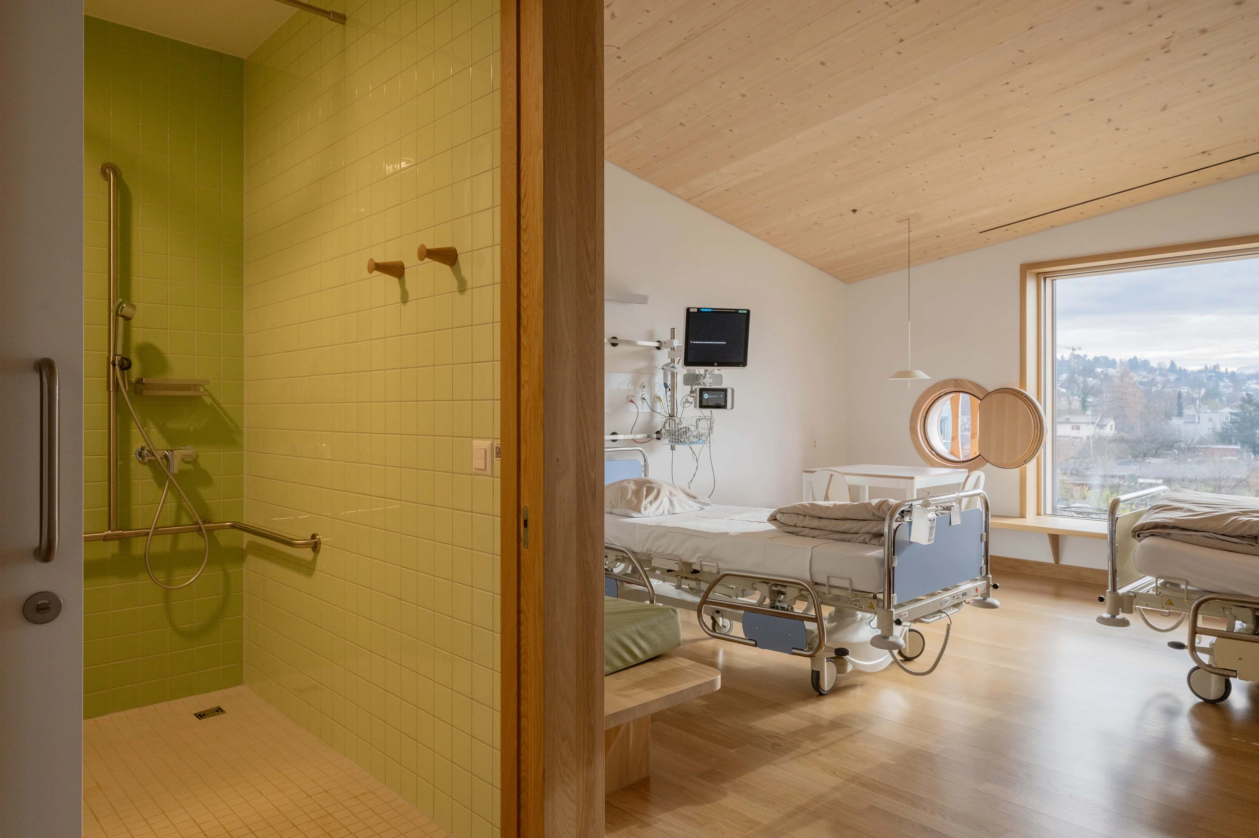 Ein Zweibett-Patientenzimmer mit Nasszelle und ausziehbareren Liegebänken für ein je ein übernachtendes Familienmitglied