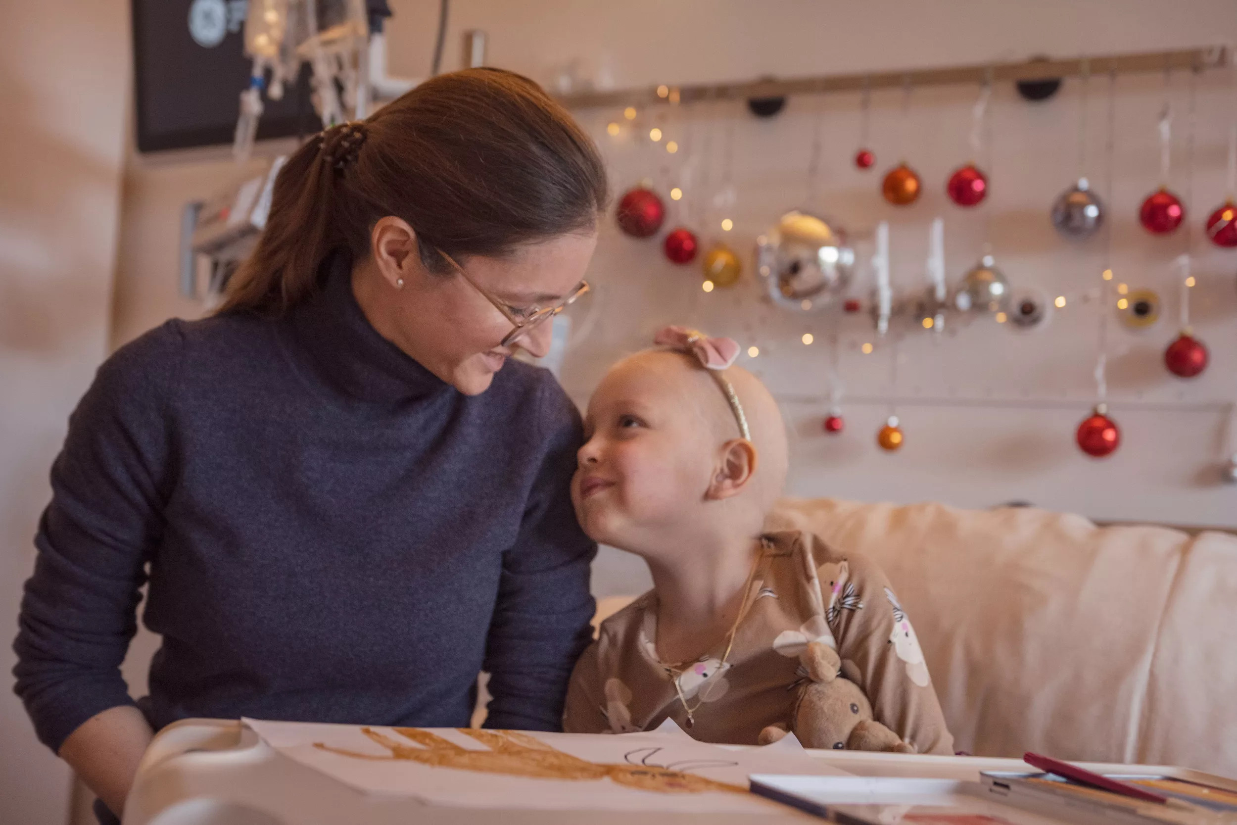 Eine Mutter und ihre junge Tochter sitzen freudig auf einem Spitalbett in einem weihnachtlich geschmückten Zimmer