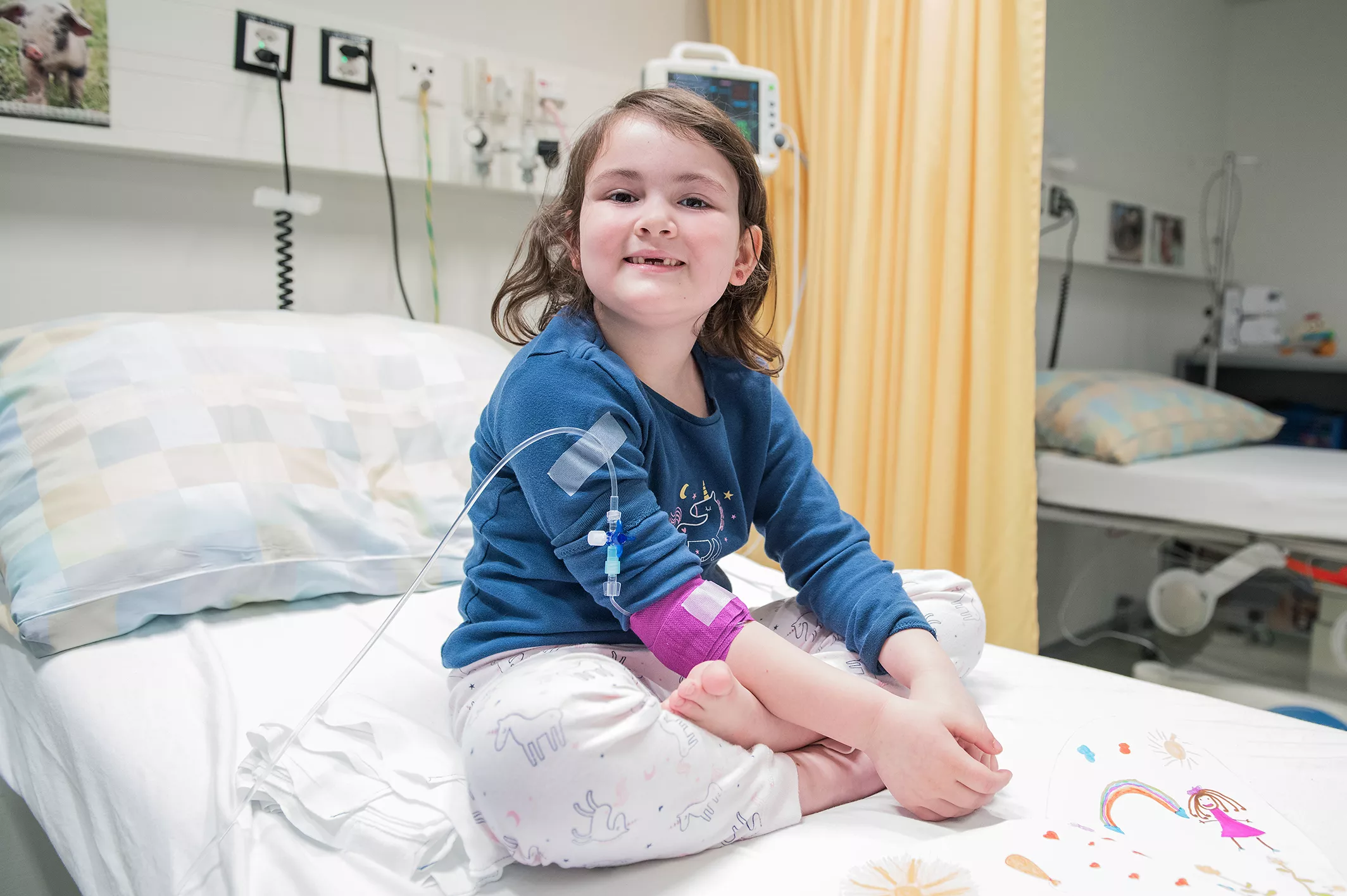 Eine Rheumapatientin sitzt im Schlafanzug auf einem Spitalbett und lächelt in die Kamera.