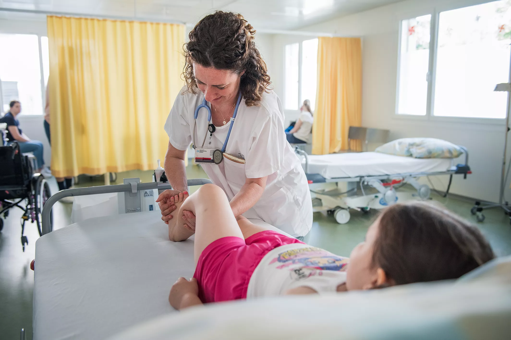 Eine Ärztin aus der Rheumatologie drückt mit ihrer Hand gegen den Fuss einer Rheumapatientin, die auf einem Spitalbett liegt.