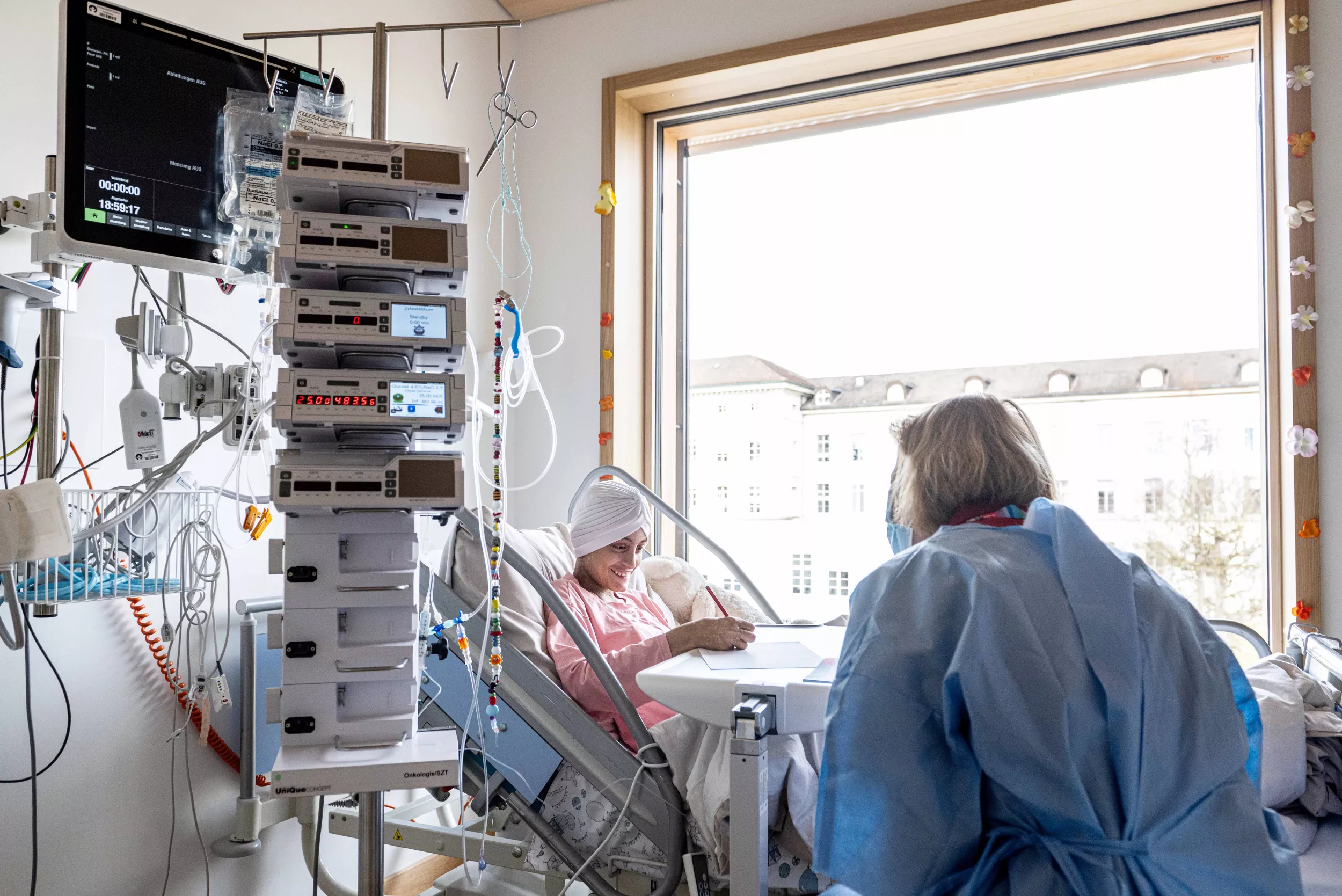 Eine Patientin liegt im Spitalbett und wird von einer Lehrerin unterrichtet