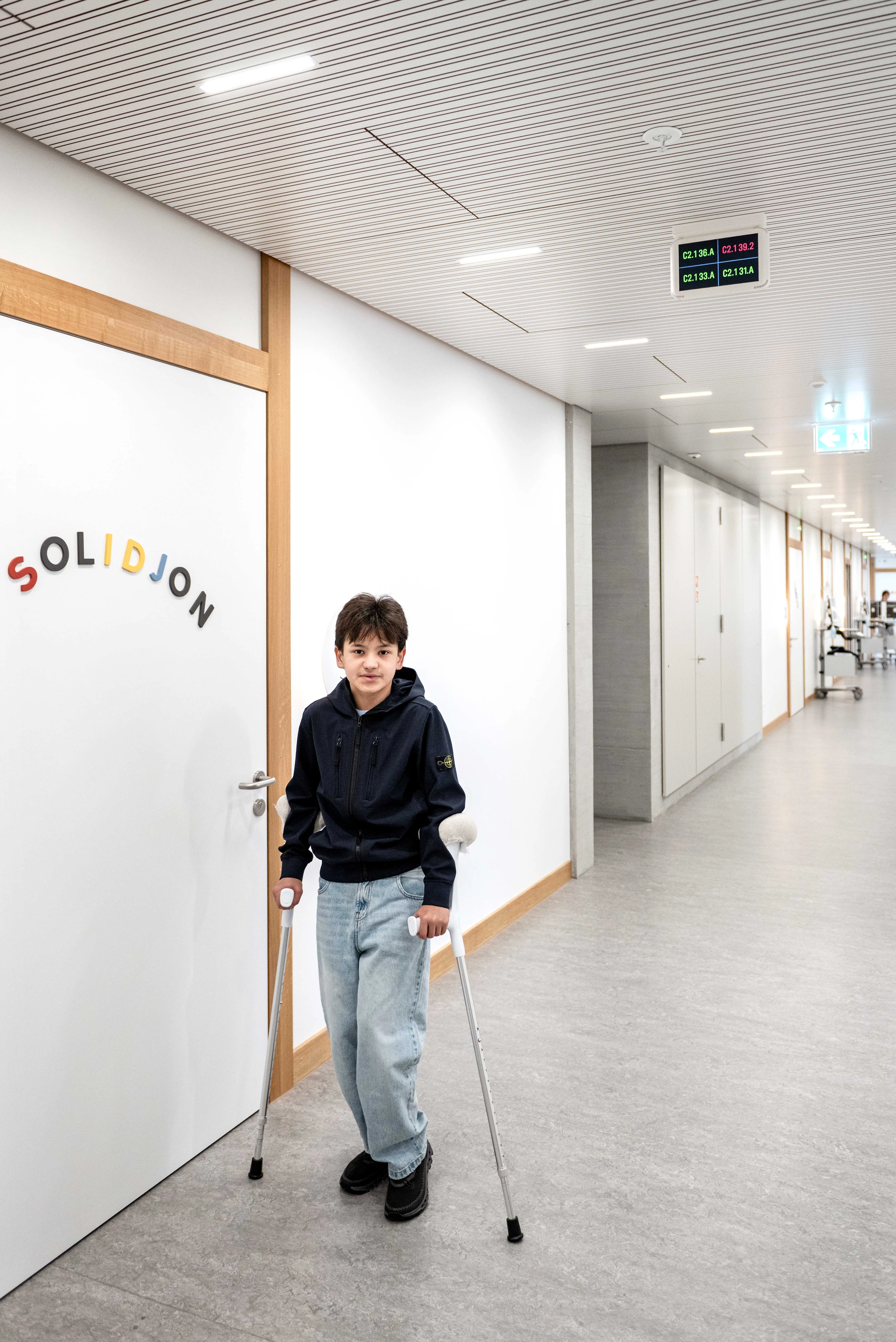 Ein Junge mit Gehstöcken steht vor einem Patientenzimmer im Kinderspital Zürich