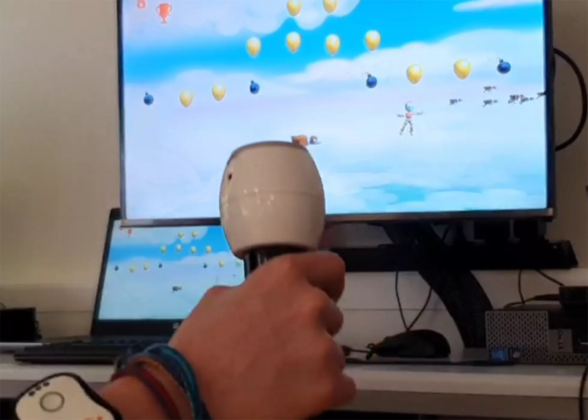 Eine Hand hält einen Joystick vor einem Bildschirm mit farbigen Punkten.