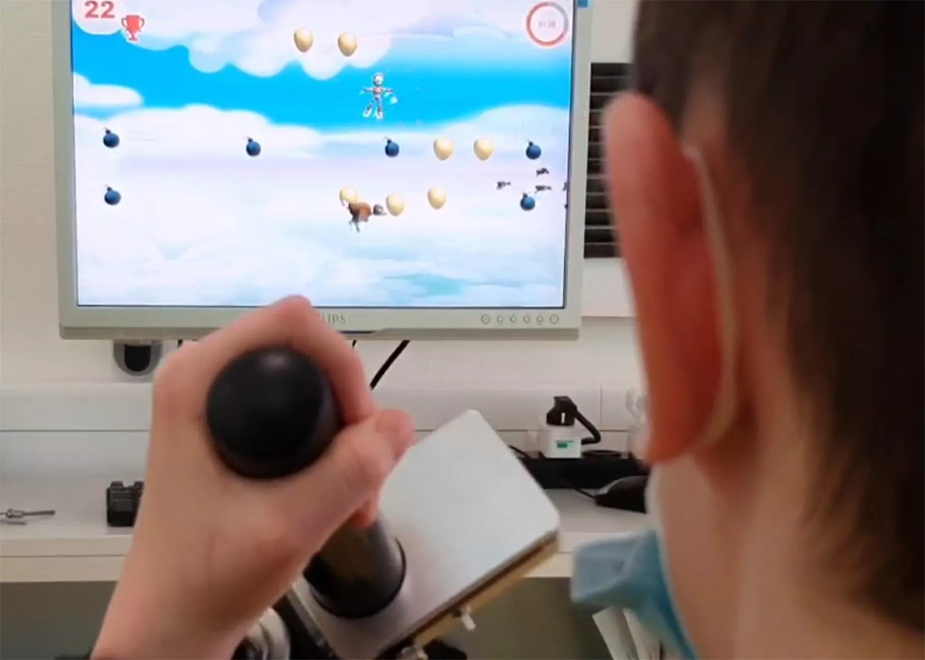 Ein Kind von hinten, es hält einen Joystick, im Hintergrund ist ein Bildschirm zu sehen.