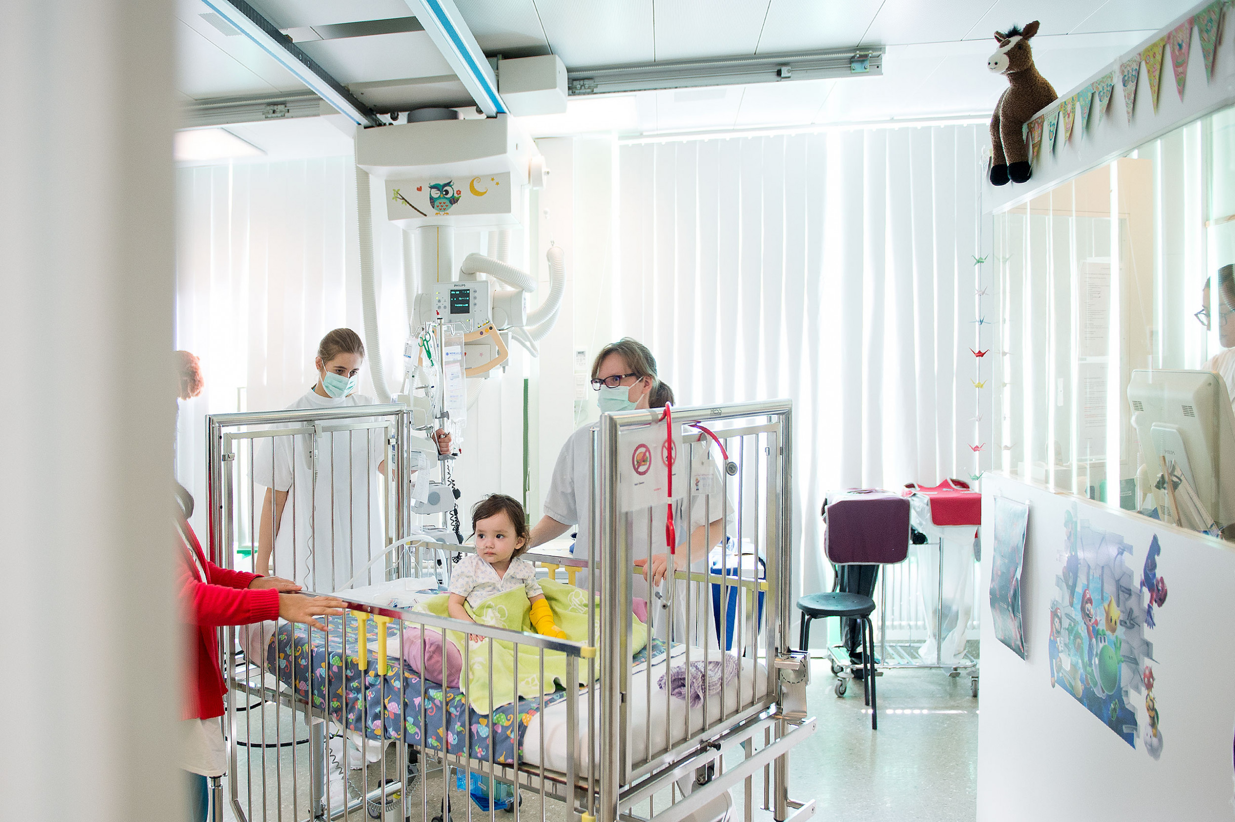 Kleines Mädchen wird von zwei Pflegefachfrauen im Spitalbett ins Röntgenzimmer gebracht