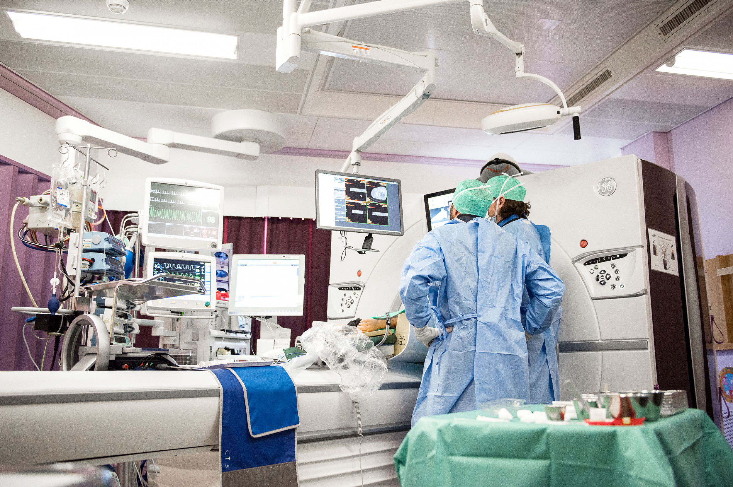 Ein chirurgischer Eingriff wird direkt im Computertomographen vorgenommen, zwei Ärzte betrachten am Bildschirm die Position der Nadel