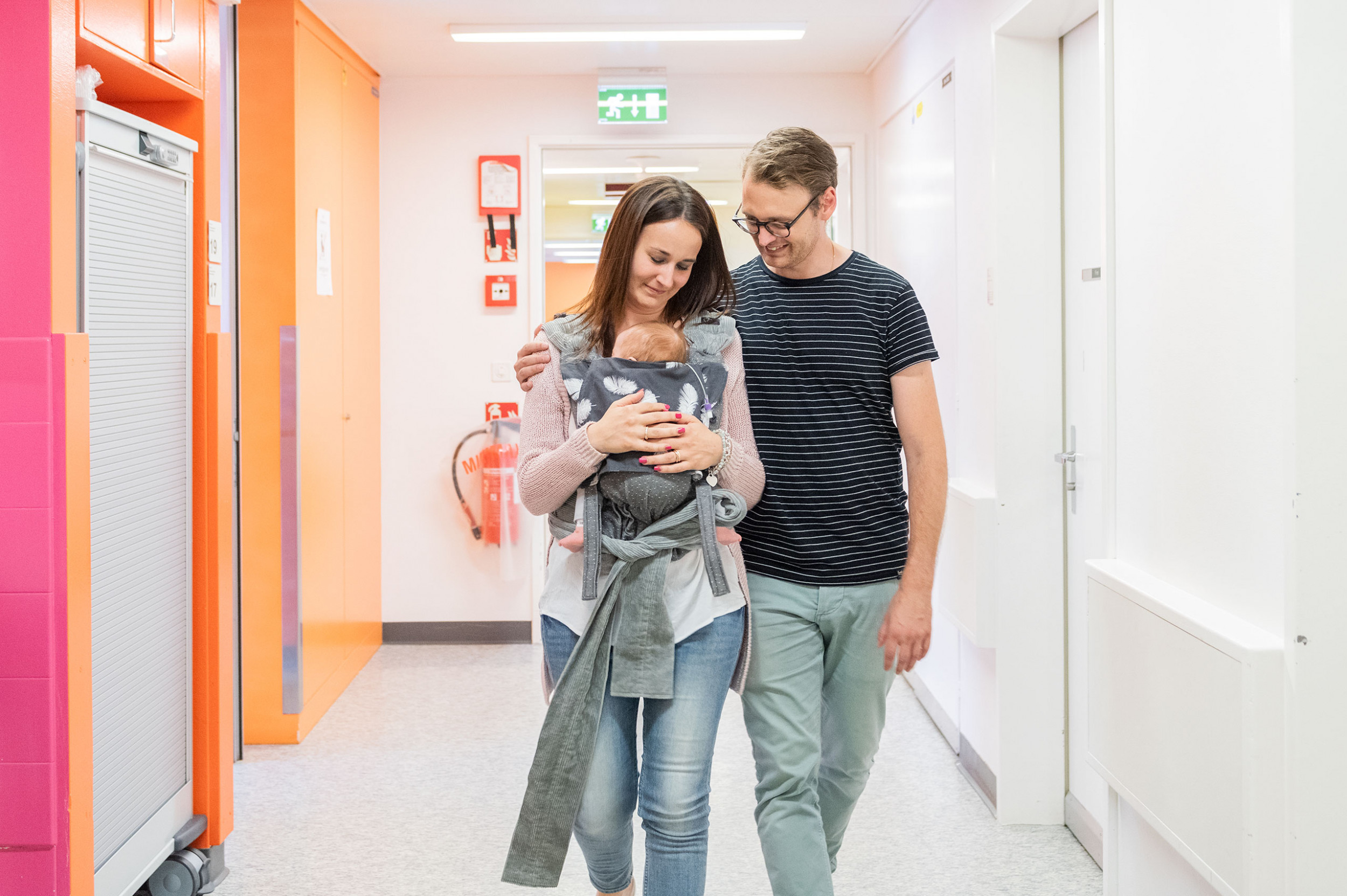 Junge Eltern laufen mit einem Baby durch den Gang des Kinderspitals