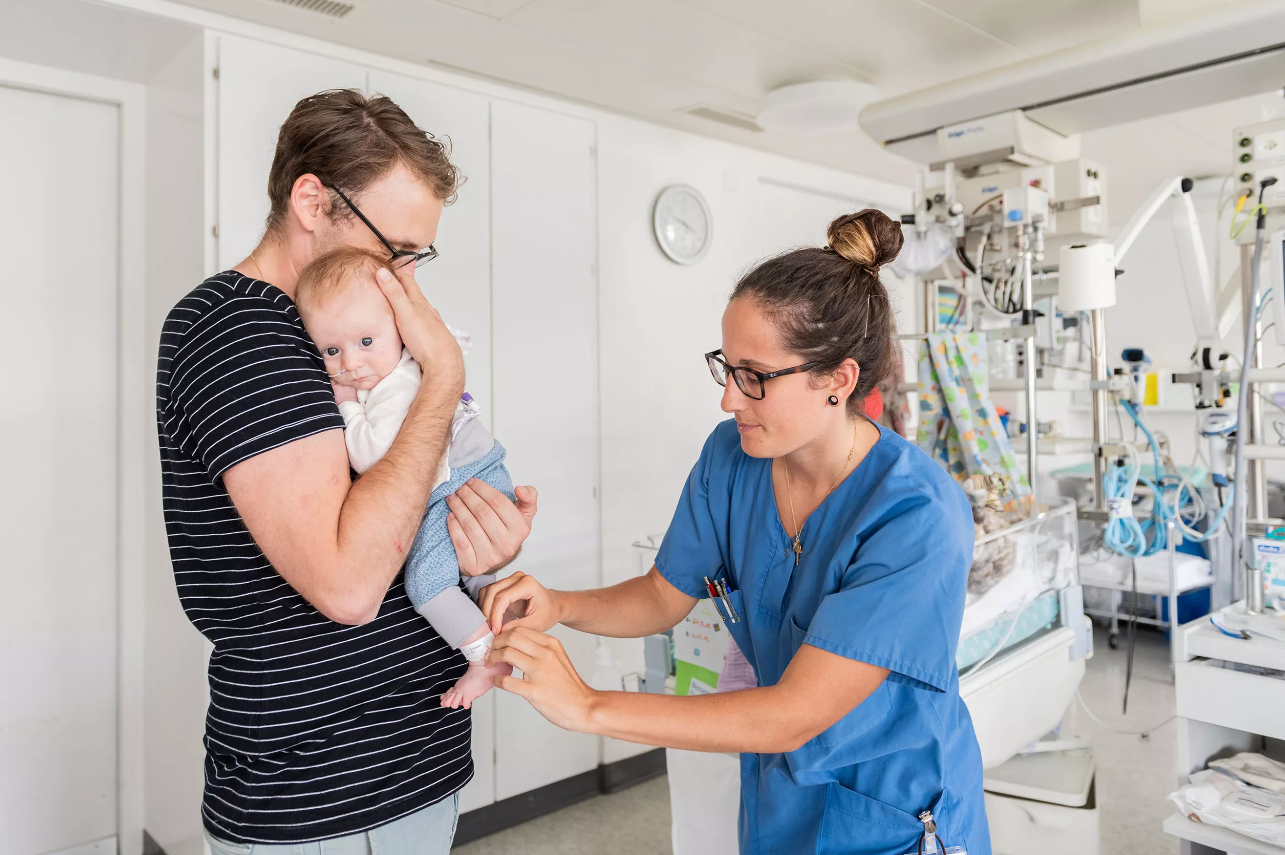 Eine Pflegefachfrau schaut zu einem Kind, während der Vater es in den Händen hält