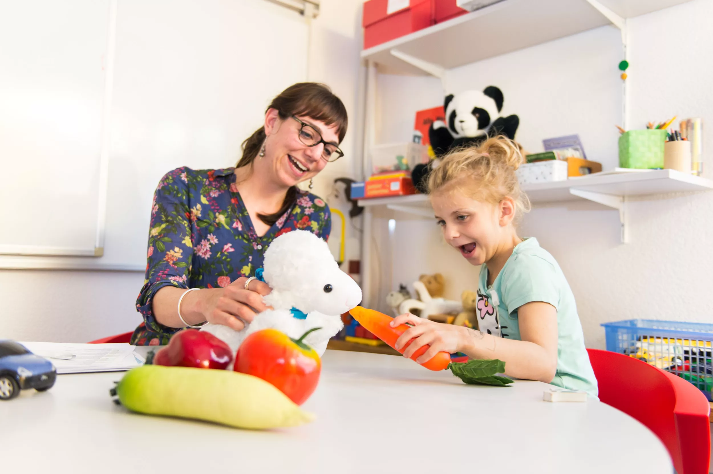 Ein Mädchen zusammen mit einer Ernährungsberaterin füttert ein Plüschtier Schaf