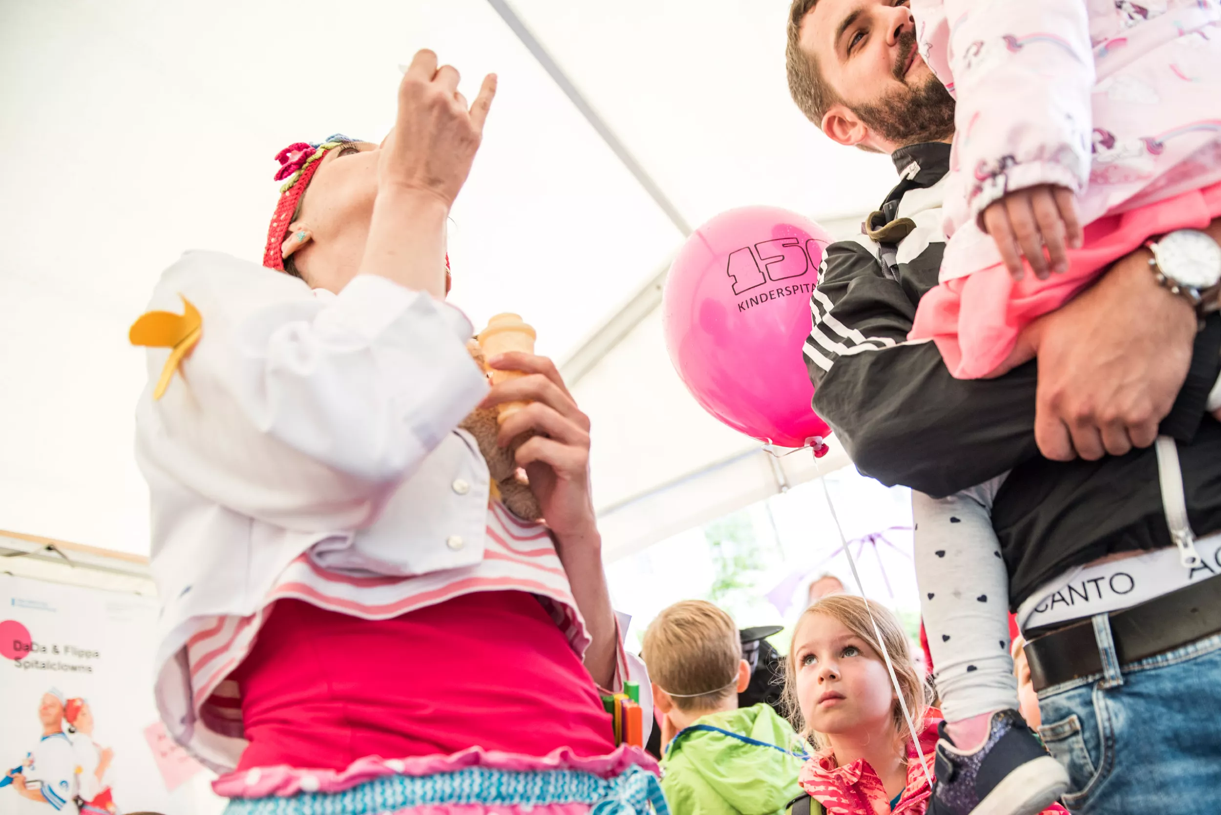 Clownin macht Seifenblasen neben Vater mit Kind 