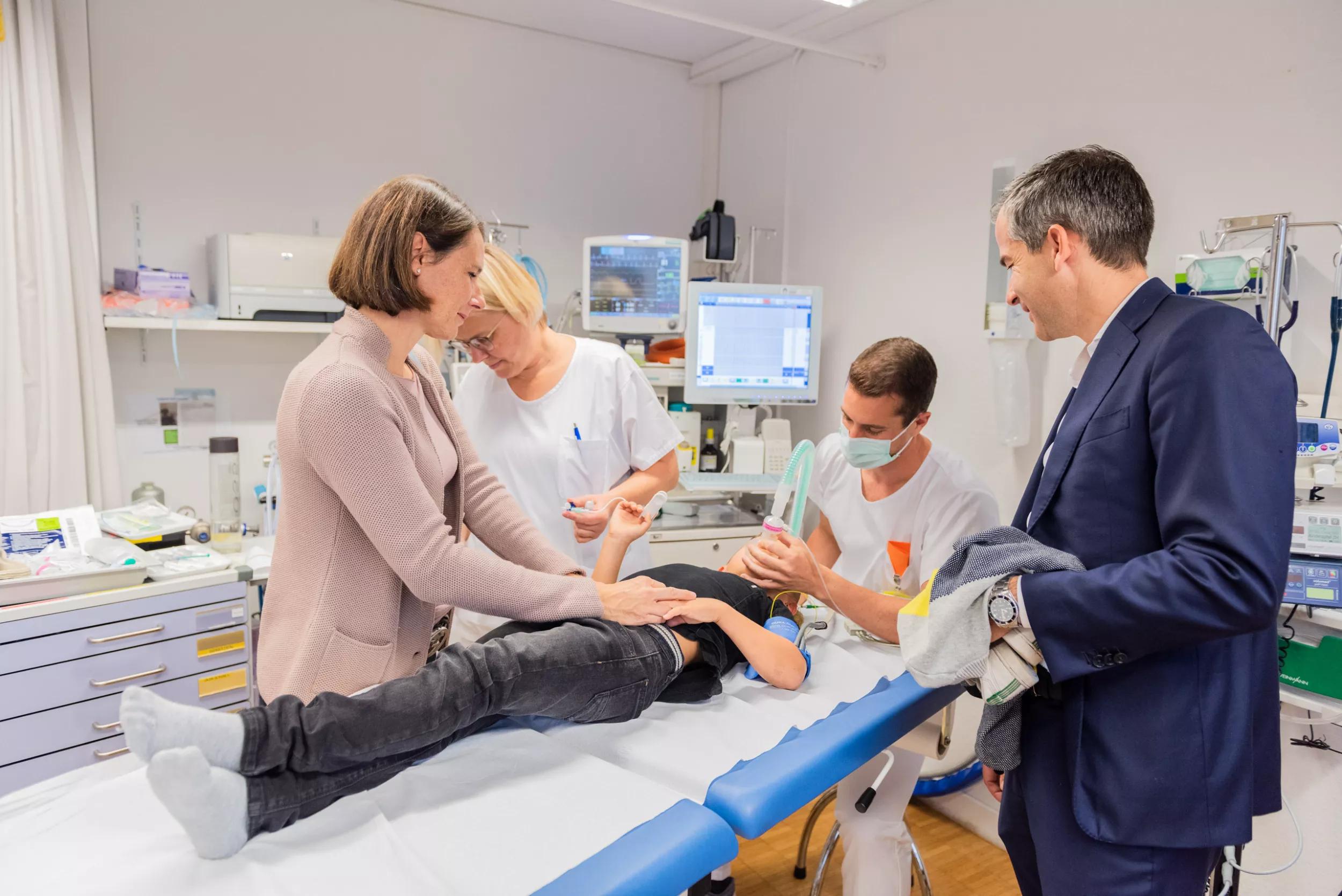 Patient wird behandelt, Eltern stehen neben ihm