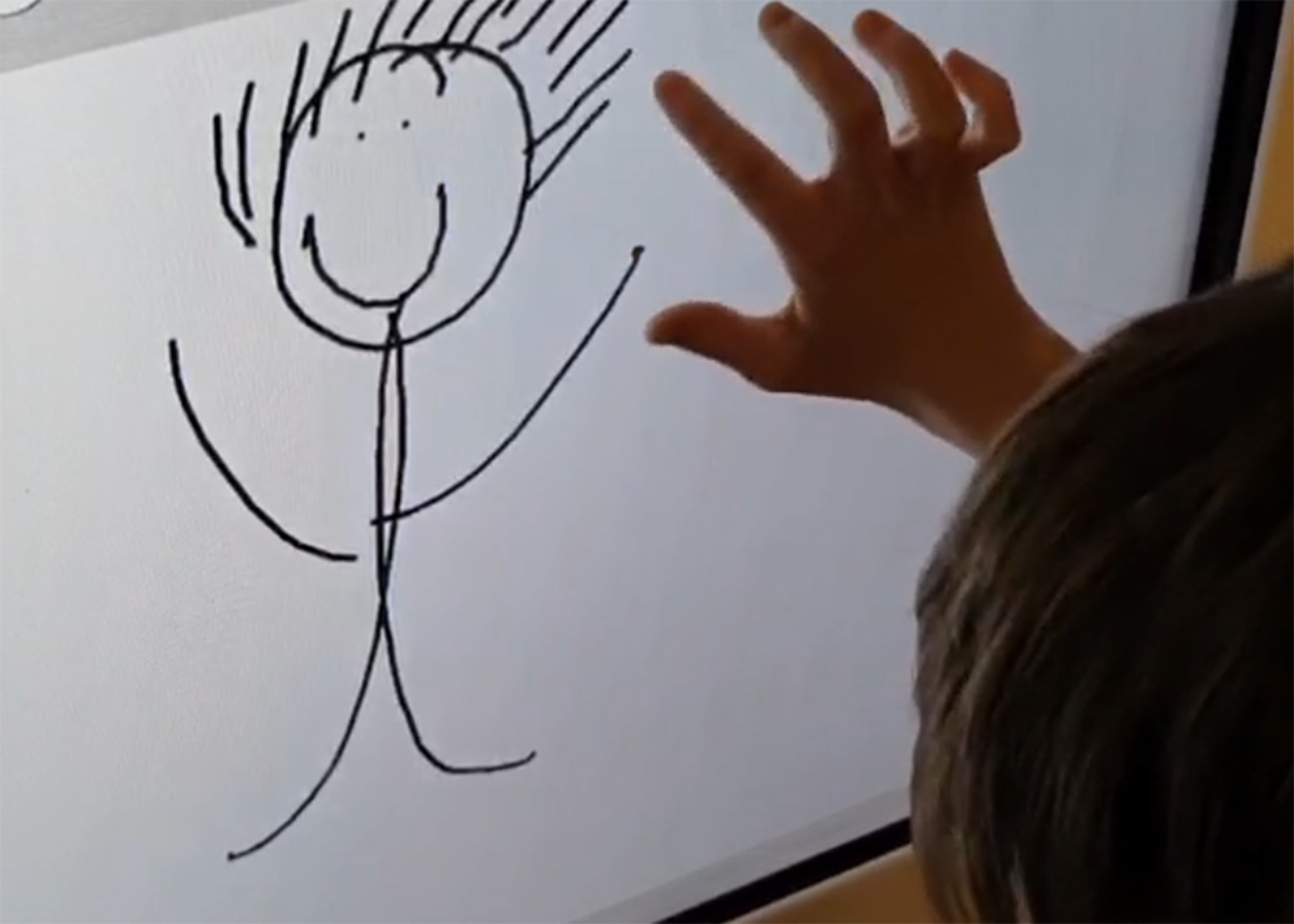 Ein Kind zeichnet mit seinem Finger ein Strichmännchen auf einem Bildschirm.