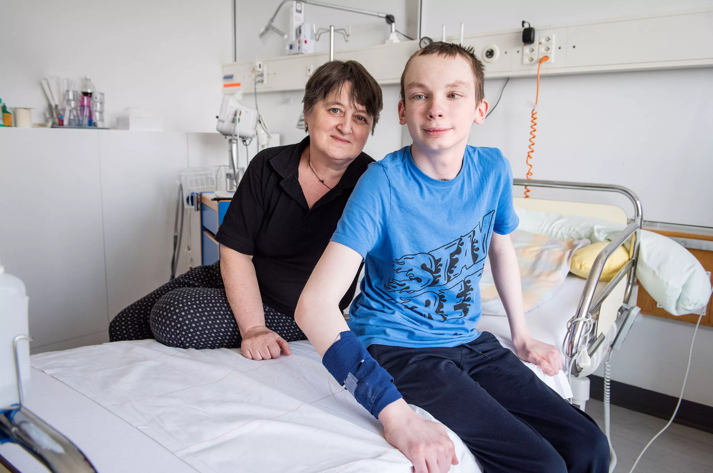 Ein Patient aus der Ukraine sitzt mit seiner Oma auf dem Bett im Spitalzimmer