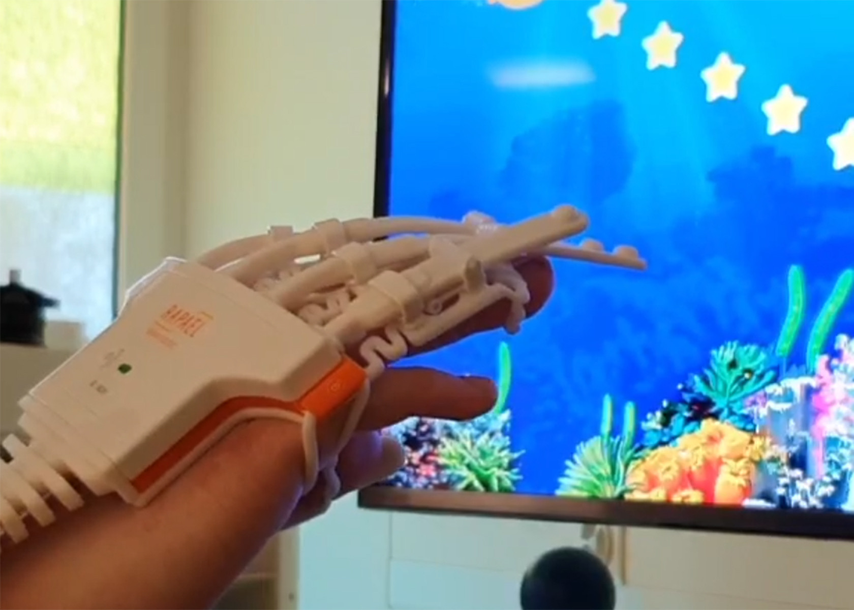 Eine Kinderhand in einer Art Roboterhand vor einem bunten Bildschirm.