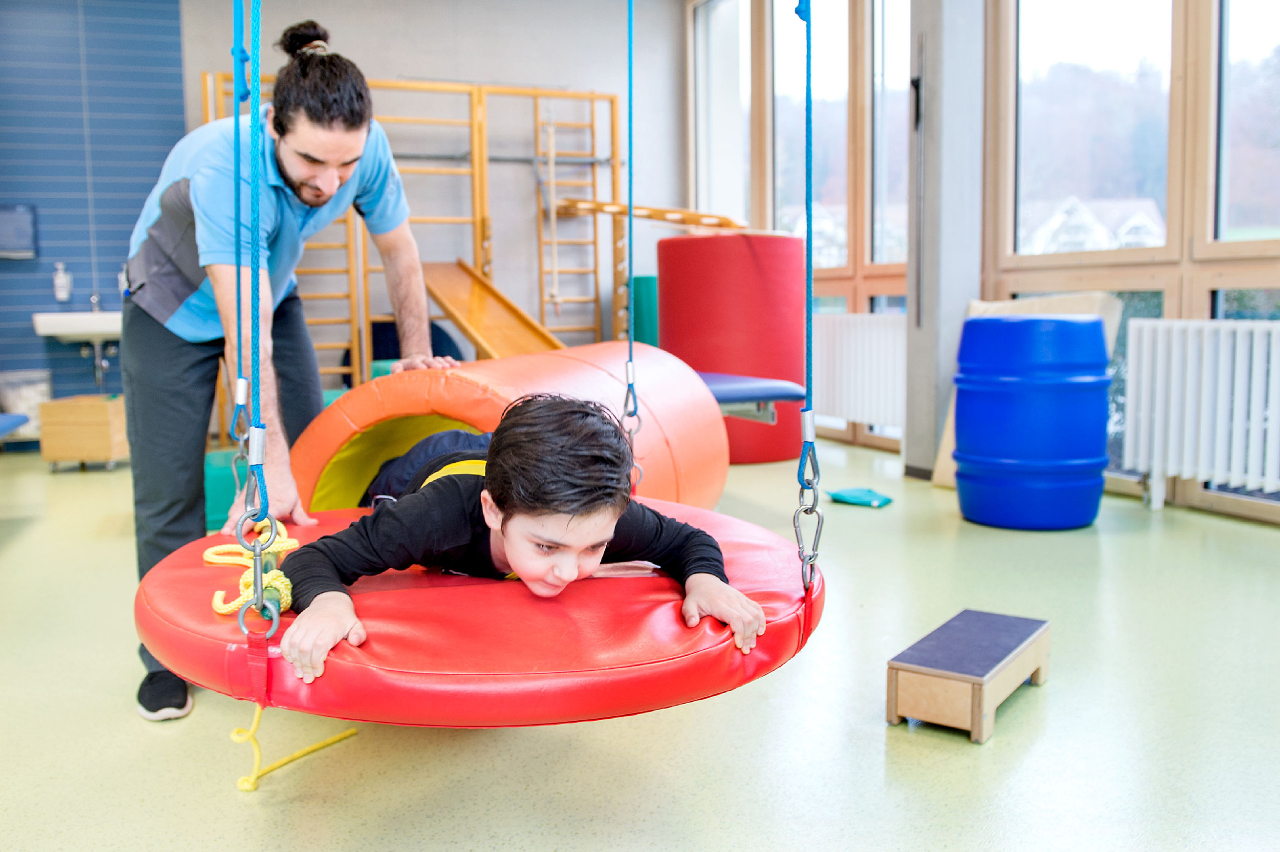 Kinder-Reha Schweiz, Physiotherapie, Therapeut mit Patient im Therapieraum beim Trainingsparcours