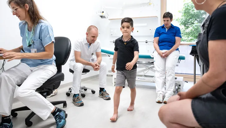 Spina-Bifida-Zentrum, Aerztin schreibt, Orthopaede beobachtet Patient beim Gehen, Pflegeexpertin beobachtet auch